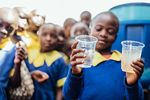 Children holding cups of water, one clear and one murky, in an outdoor setting.