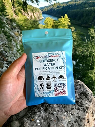 Hand holding an emergency water purification kit package with scenic river background.