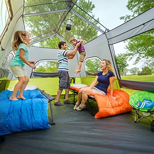 Family enjoying time inside a large camping tent with sleeping bags and chairs.