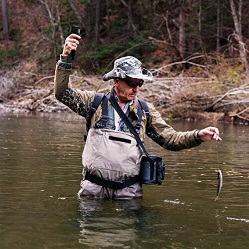 Man in waders fishing in a river with a catch.