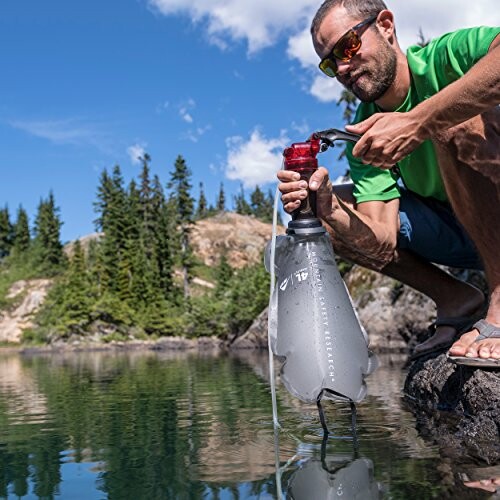 Man using a water purifier by a lake in a natural setting.