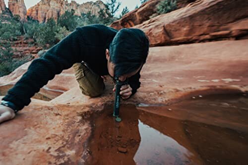 Person examining water in rocky terrain using a tool.